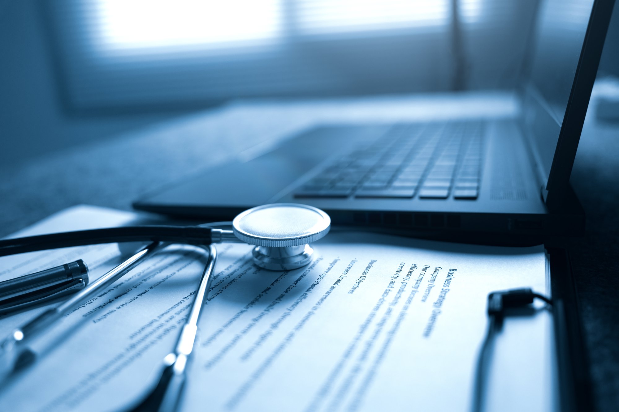 a laptop, stethoscope and paper on a desk.