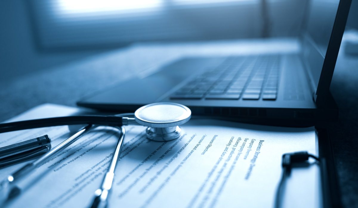 a laptop, stethoscope and paper on a desk.