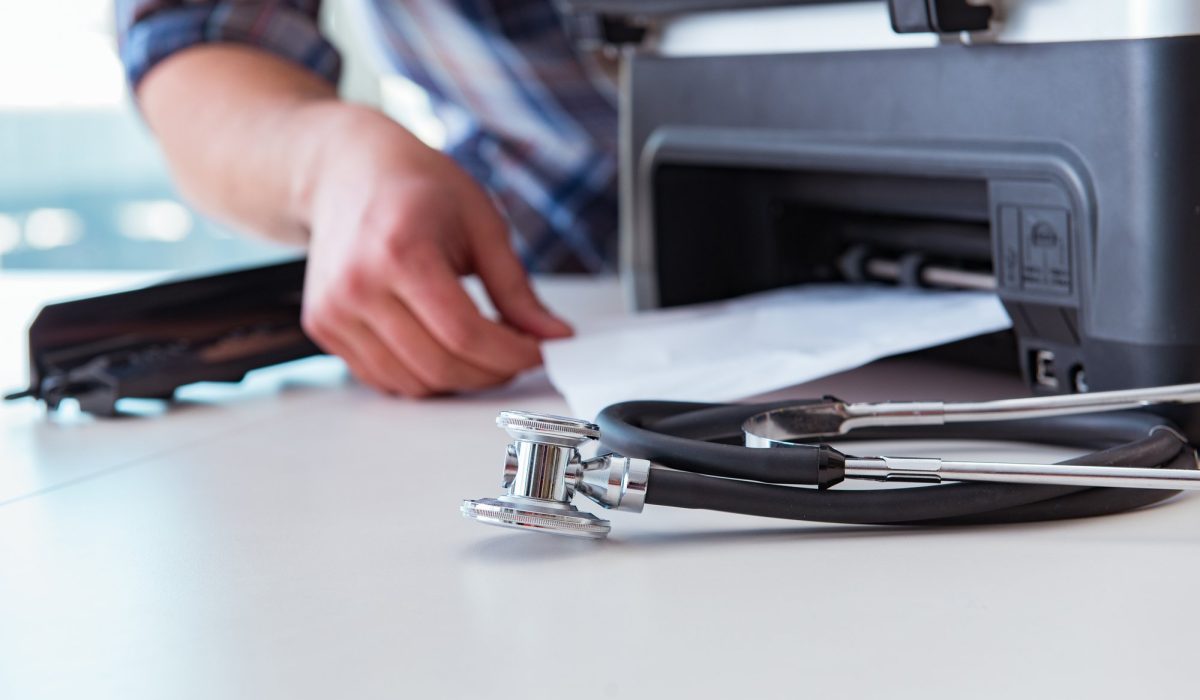 a desk with a stethoscope and a printer. a hand is retrieving a paper in the printer.